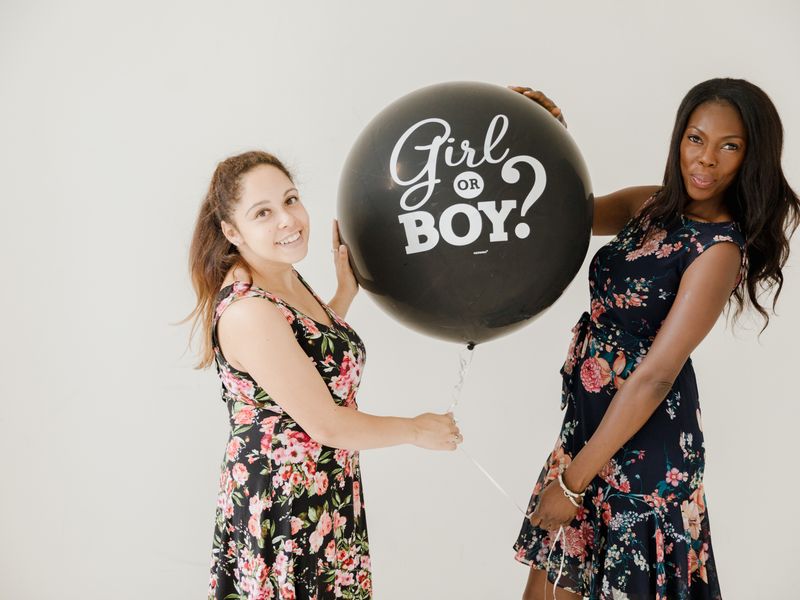 Two women holding a black gender reveal balloon