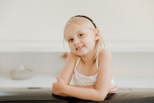 A cheerful young girl with a headband smiling indoors, captured in a bright setting.