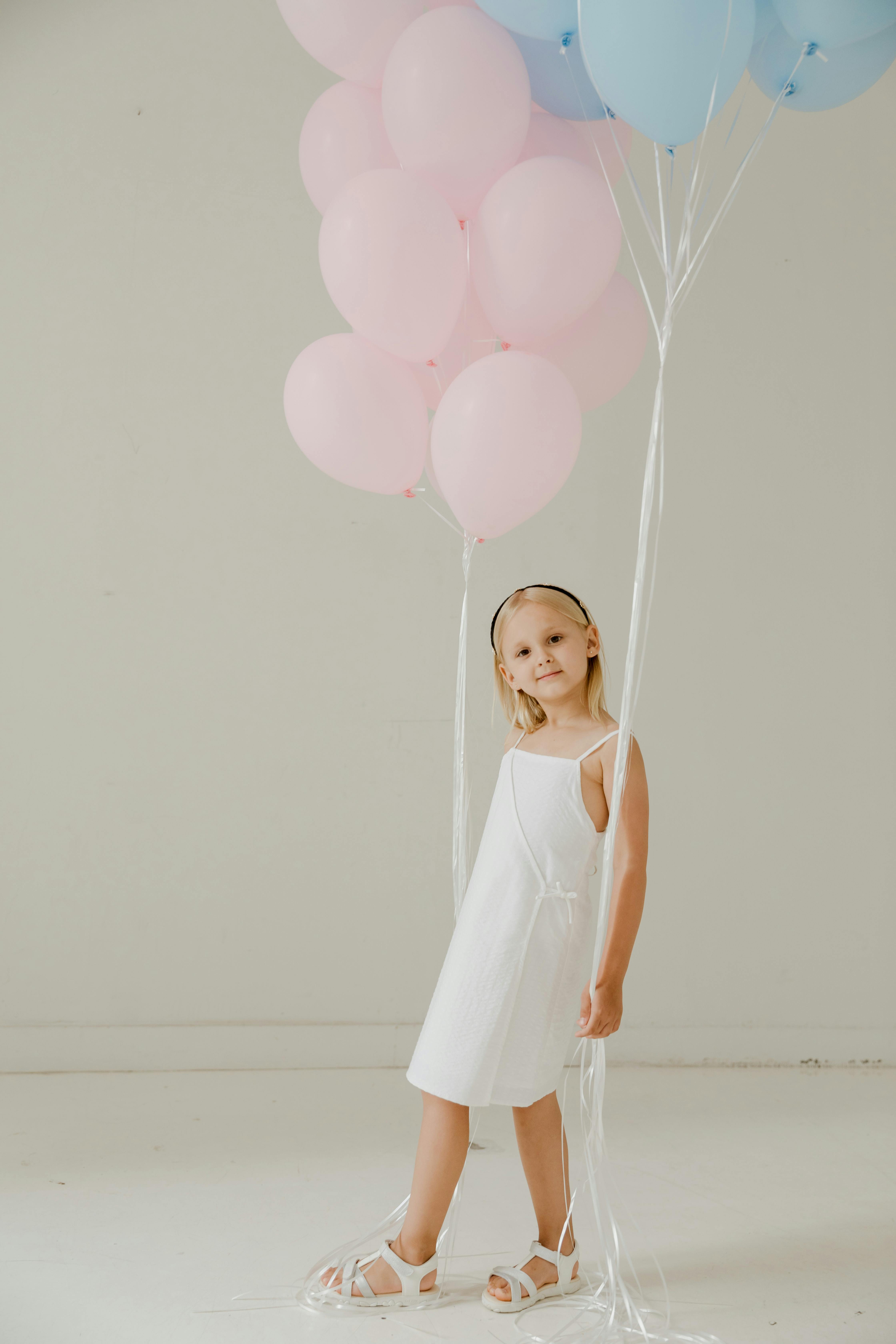 a girl in white dress holding pink and blue balloons