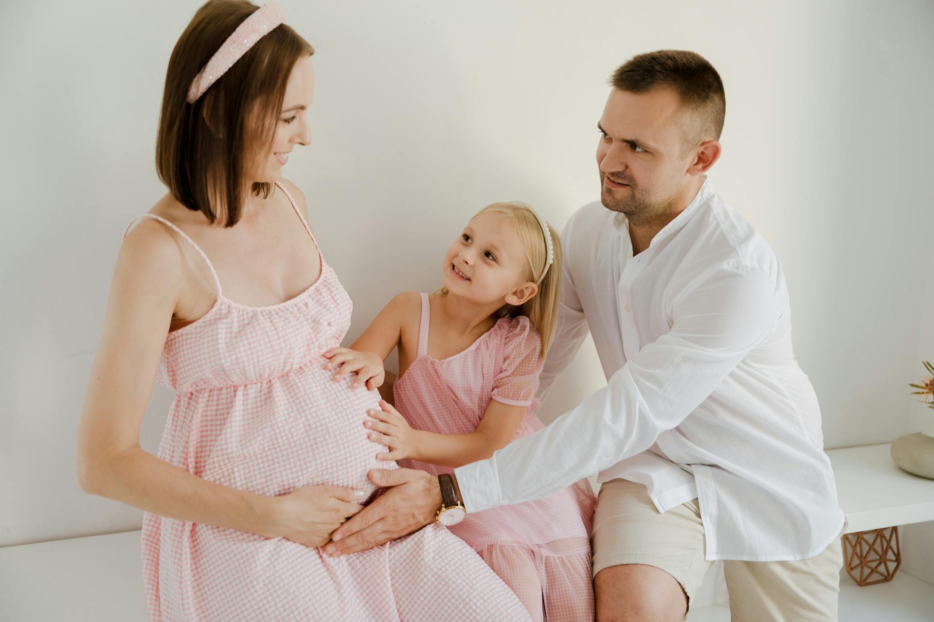 En far och hans dotter rör vid den gravida moderns babybump