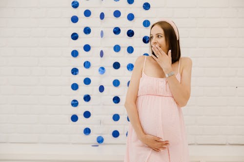 Free Pregnant Woman in Pink Dress Leaning on a Wall with Dots Stock Photo
