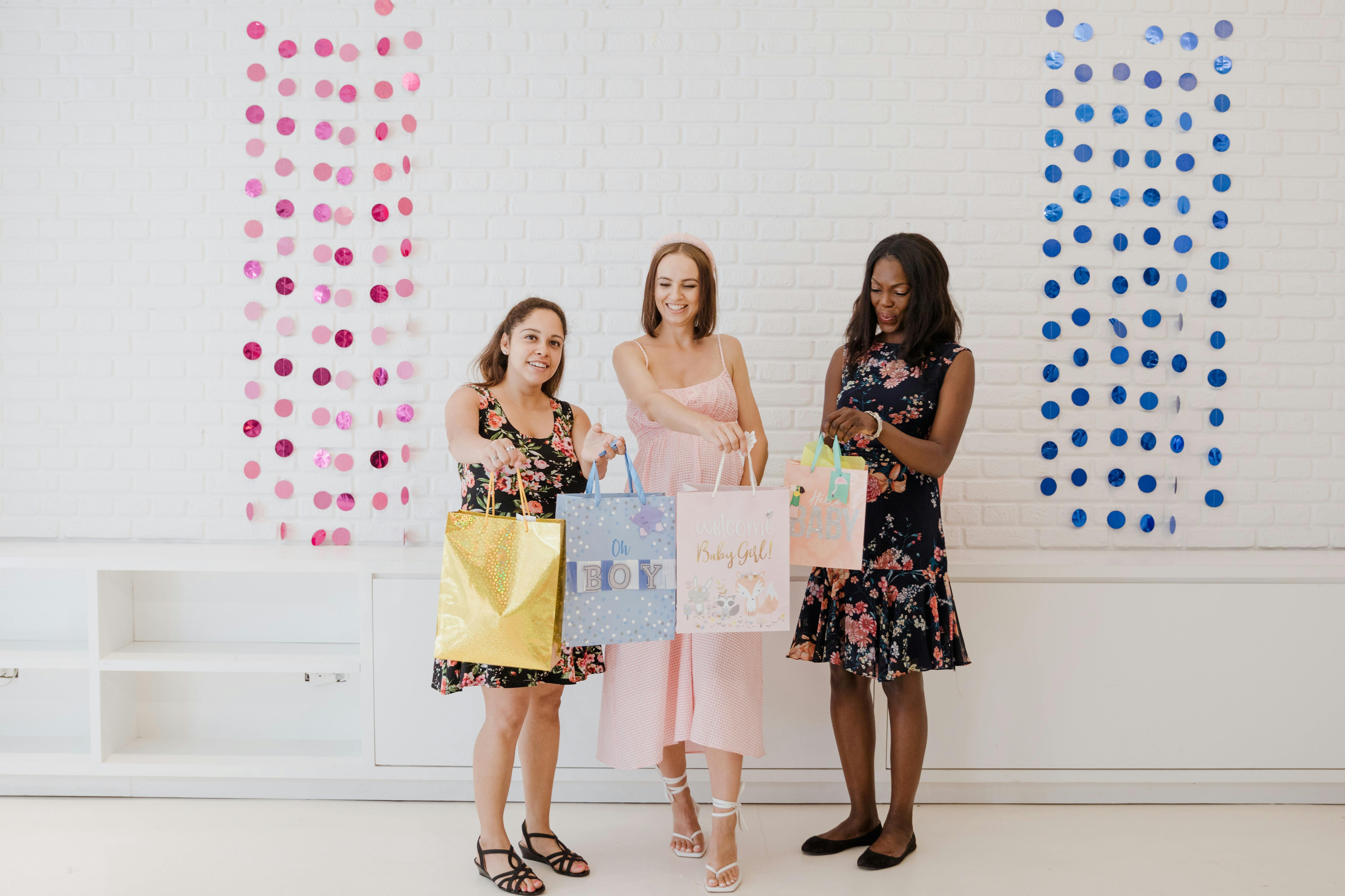 Three women celebrating a baby shower with colorful gift bags and decorations.