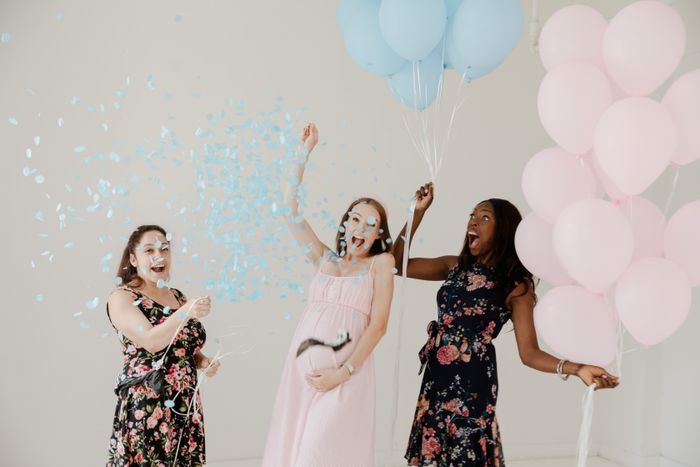 Friends celebrating a gender reveal with balloons and confetti