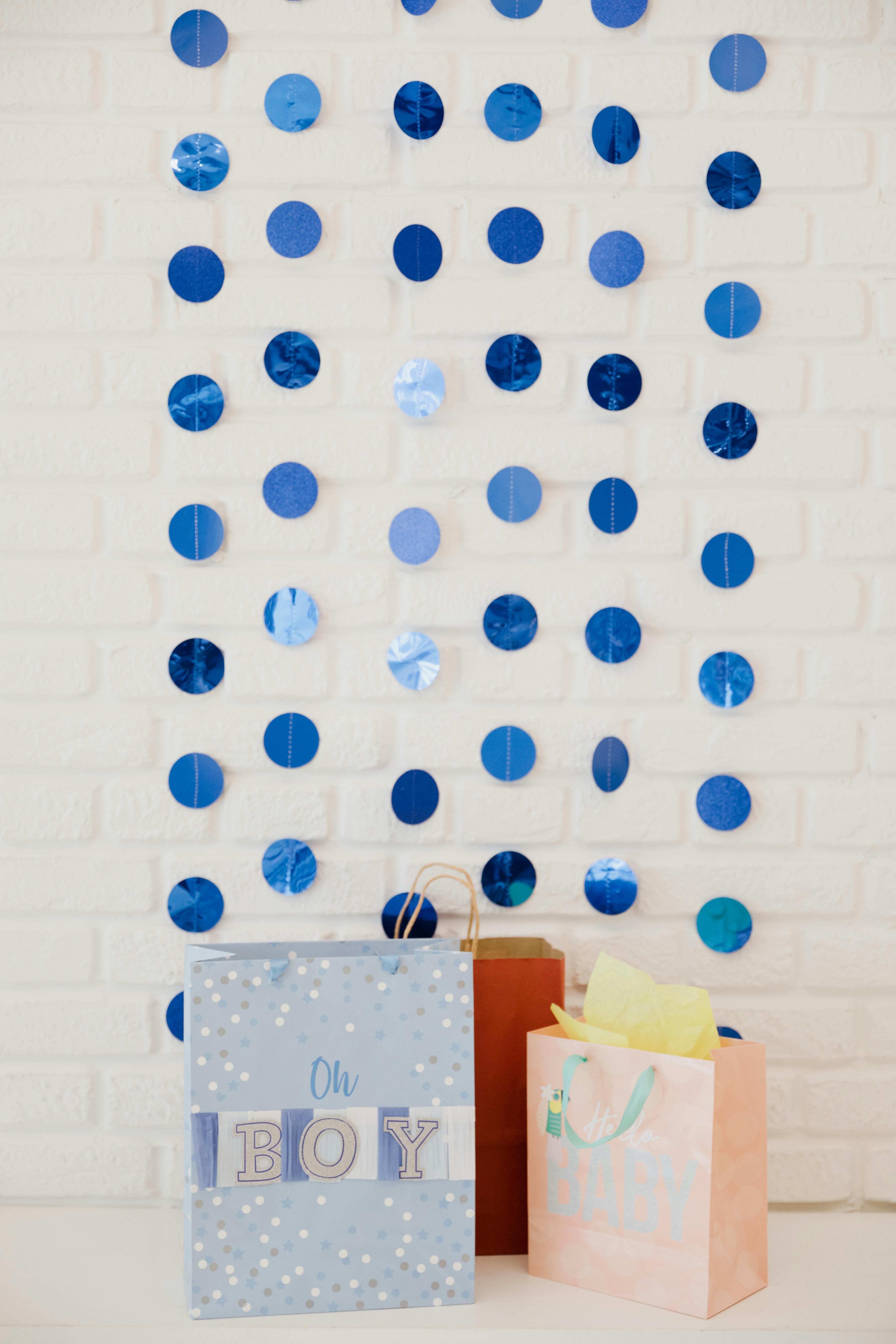 Gift bags with blue circle decorations on white brick wall at baby shower.
