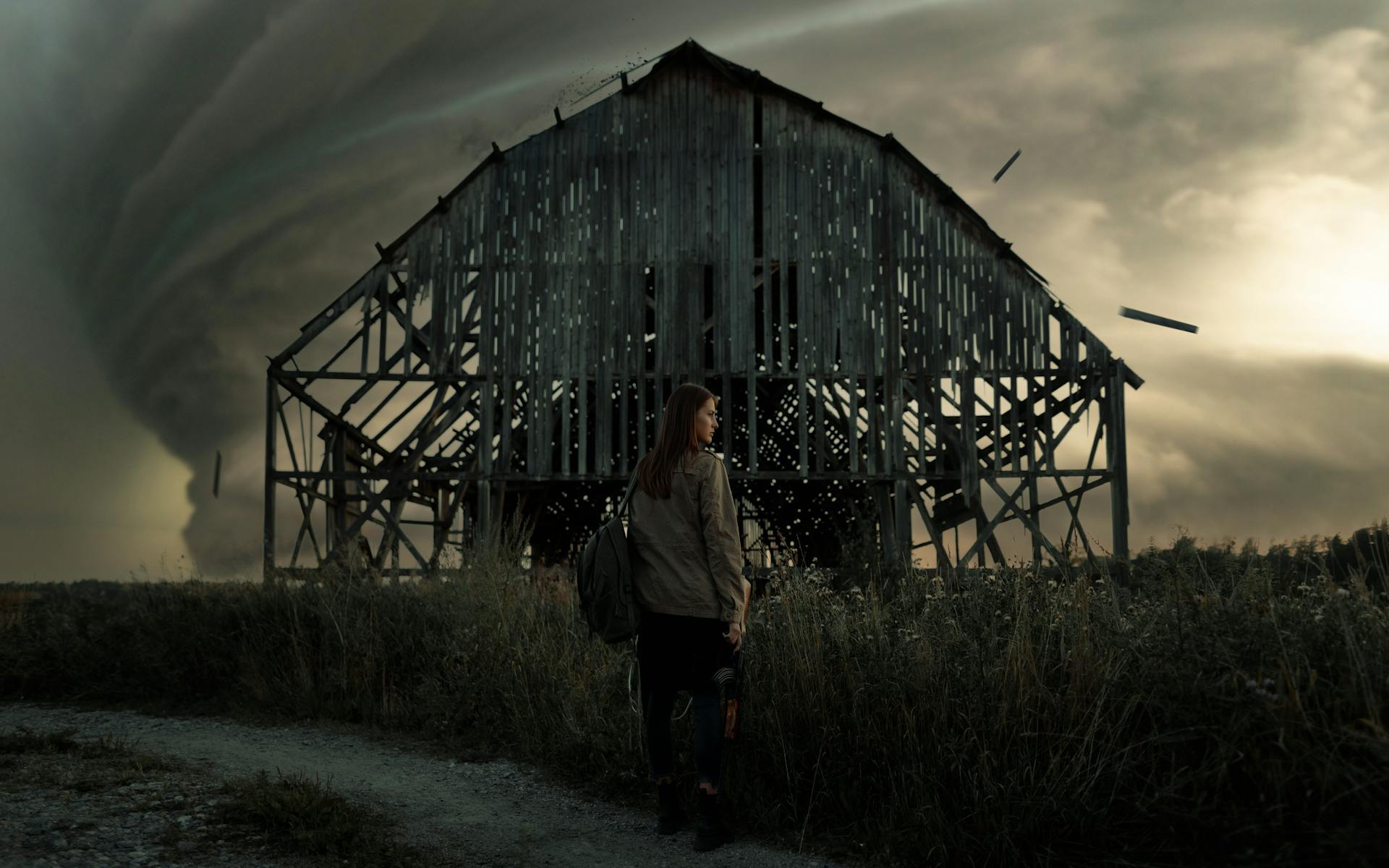 A tense moment with a woman standing before an impending tornado near a decrepit barn.