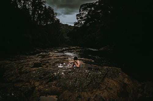 Naked Person Sitting on Rocky Riverside