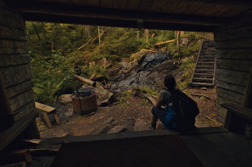 Woman with Backpack Sitting on Shed Wall in Forest