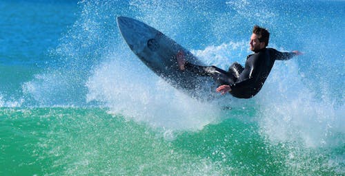 A Man in Black Wetsuit Surfing on Water