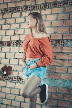 Confident young woman in casual outfit posing against an urban brick wall, embodying modern street style.