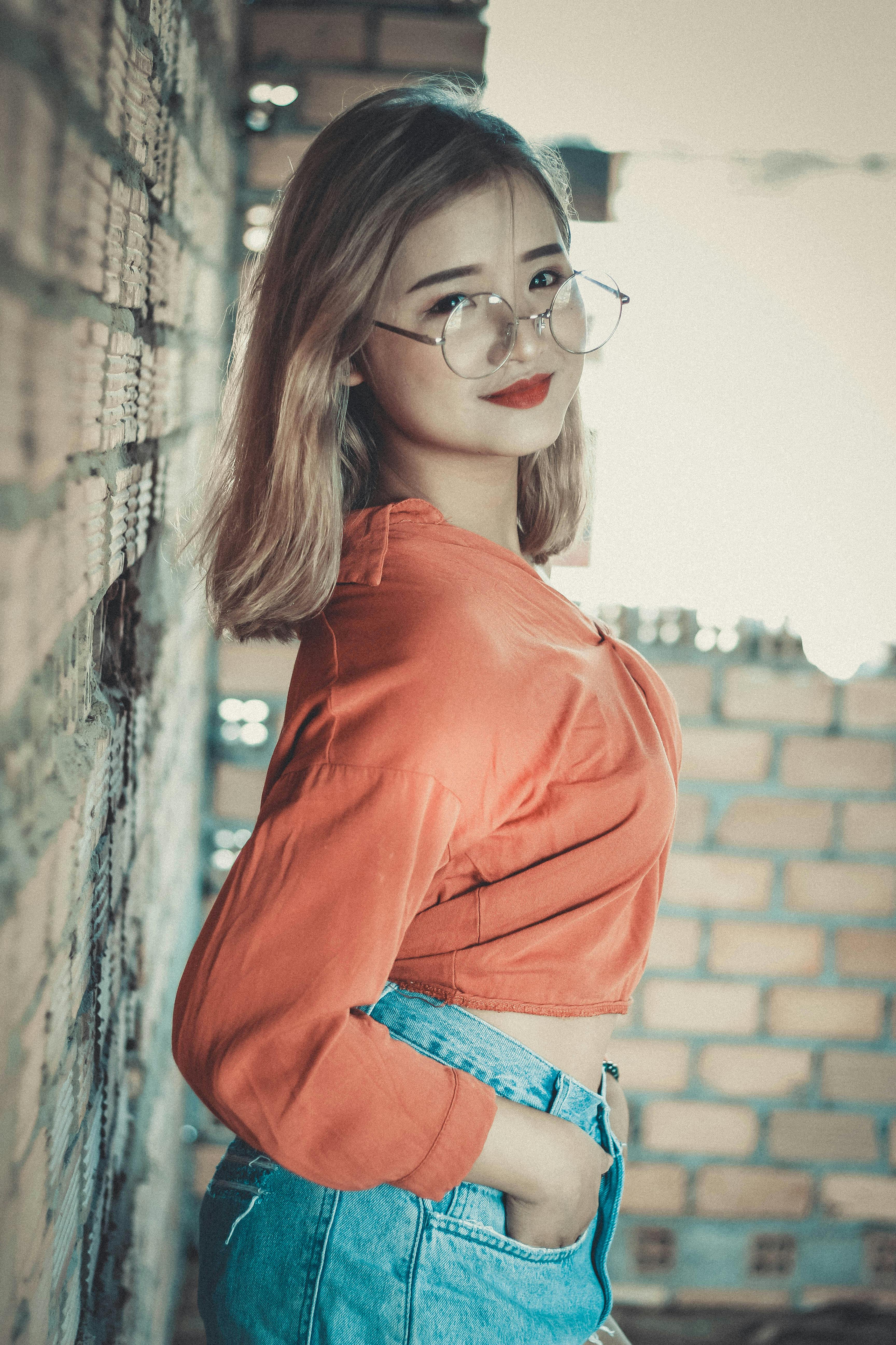 Portrait of pretty stylish teen girl wearing glasses, jeans jacket and gray  dress in front of brick wall Stock Photo