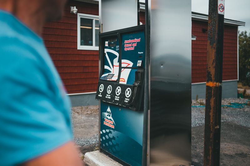 A close-up of a gas pump with a person nearby in Newfoundland, outdoors.