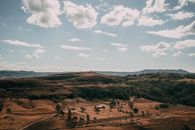 Explore the tranquility of a scenic landscape featuring rolling brown hills, lush green valleys, and a clear blue sky with white clouds.