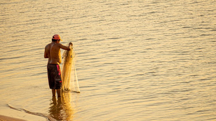 Man With Fishing Net In Water On Sunset