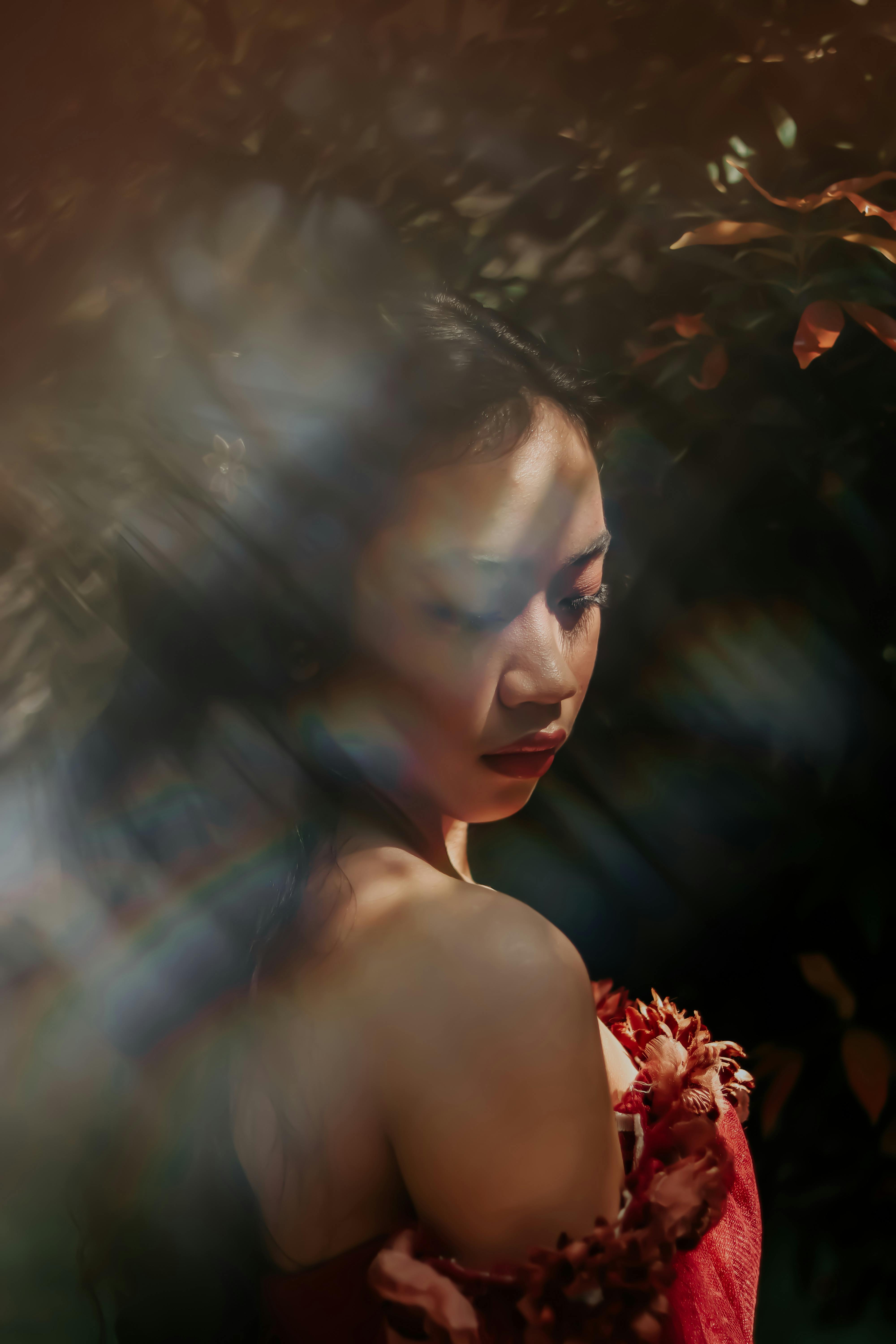 Elegant portrait of an Asian woman in a garden with dramatic lighting, wearing a red dress.