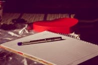 一个心形盒子上放着一支笔，旁边是一本螺旋笔记本，象征着爱情与写作