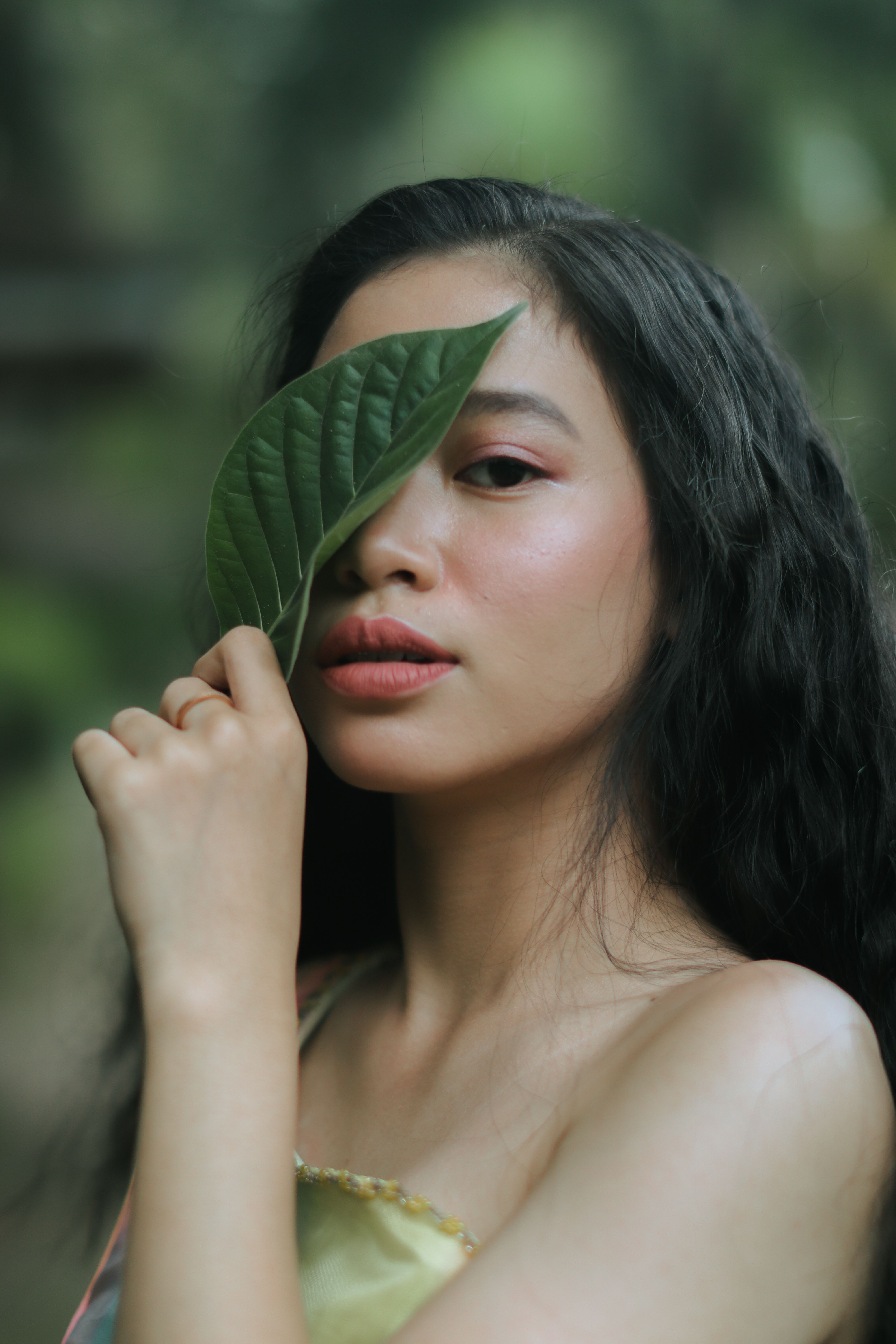 A creative portrait of a woman holding a leaf near her face in a natural setting.
