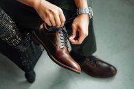 Close-up view of a man's hands tying brown leather shoes indoors.