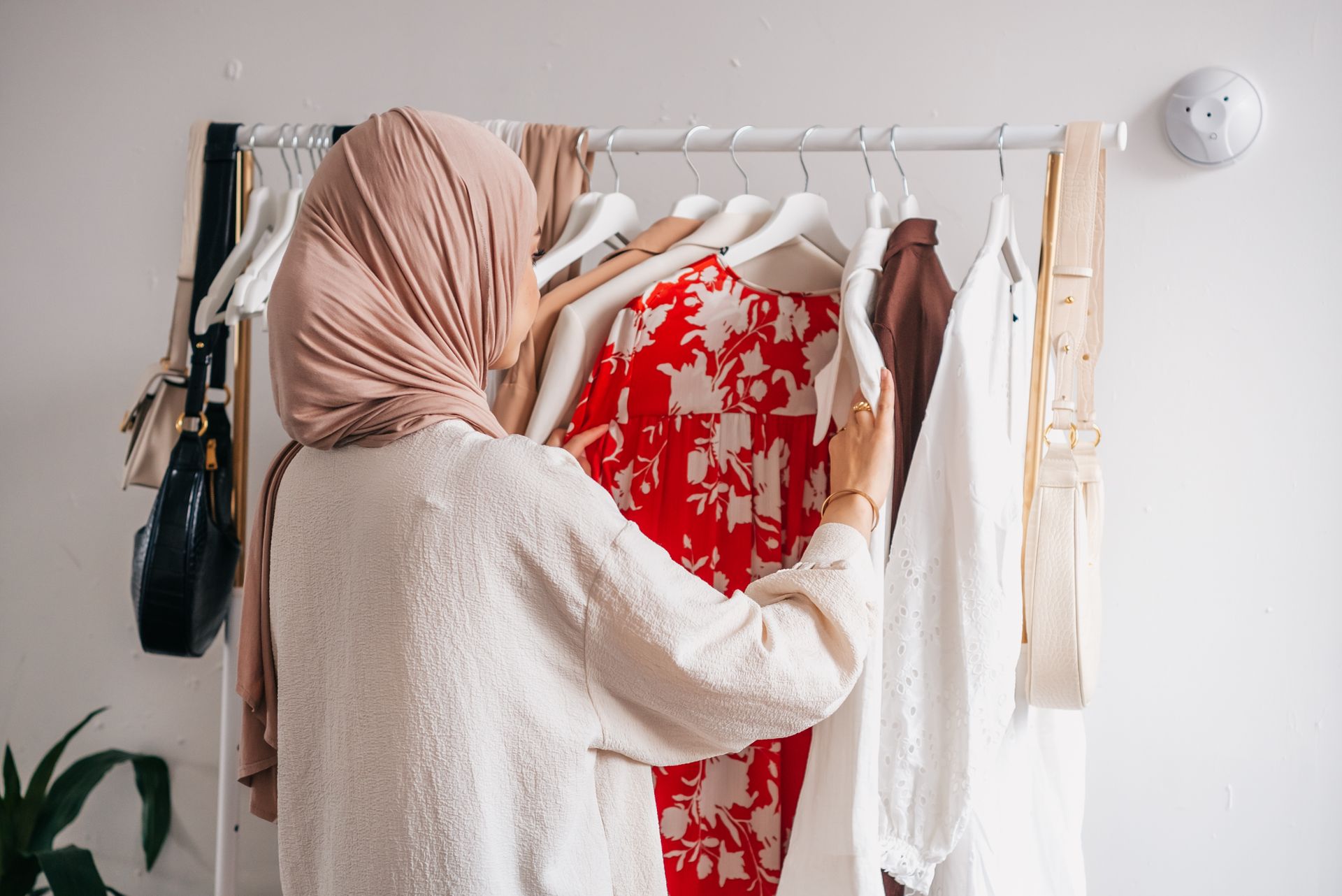 Woman in hijab organizing wardrobe, selecting various clothing options indoors.