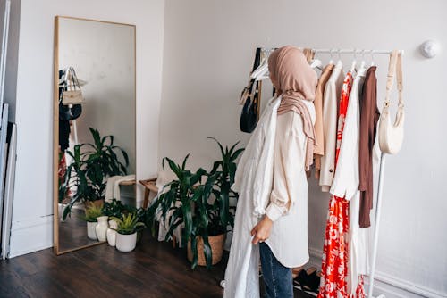 Woman Wearing Hijab Looking at Mirror While Holding a Dress