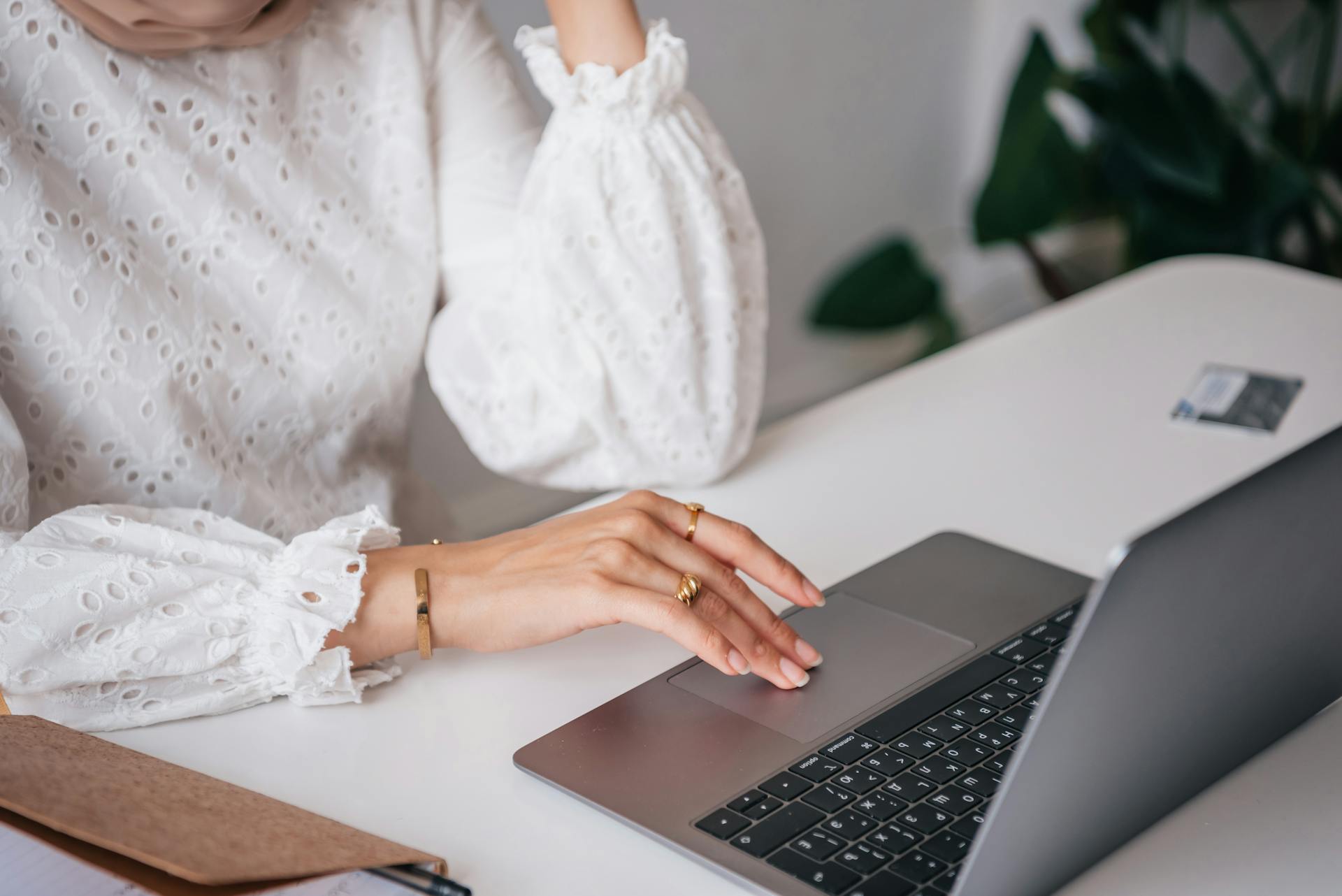 Close-up of a woman's hand with gold rings using a laptop touchpad in a stylish workspace.