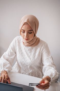 Young woman in hijab using a credit card for online shopping indoors.