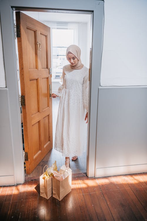 Woman Standing in the Doorway of an Apartment and Looking at Paper Bags Left on the Doorstep 