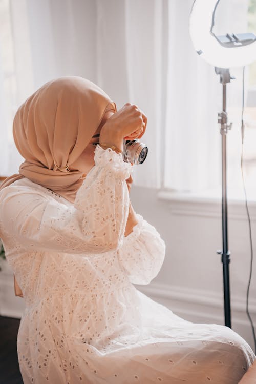 Woman in Hijab and White Dress Sitting and Taking Pictures