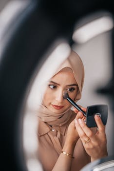 Woman in hijab applying makeup with a brush in a close-up indoor setting.