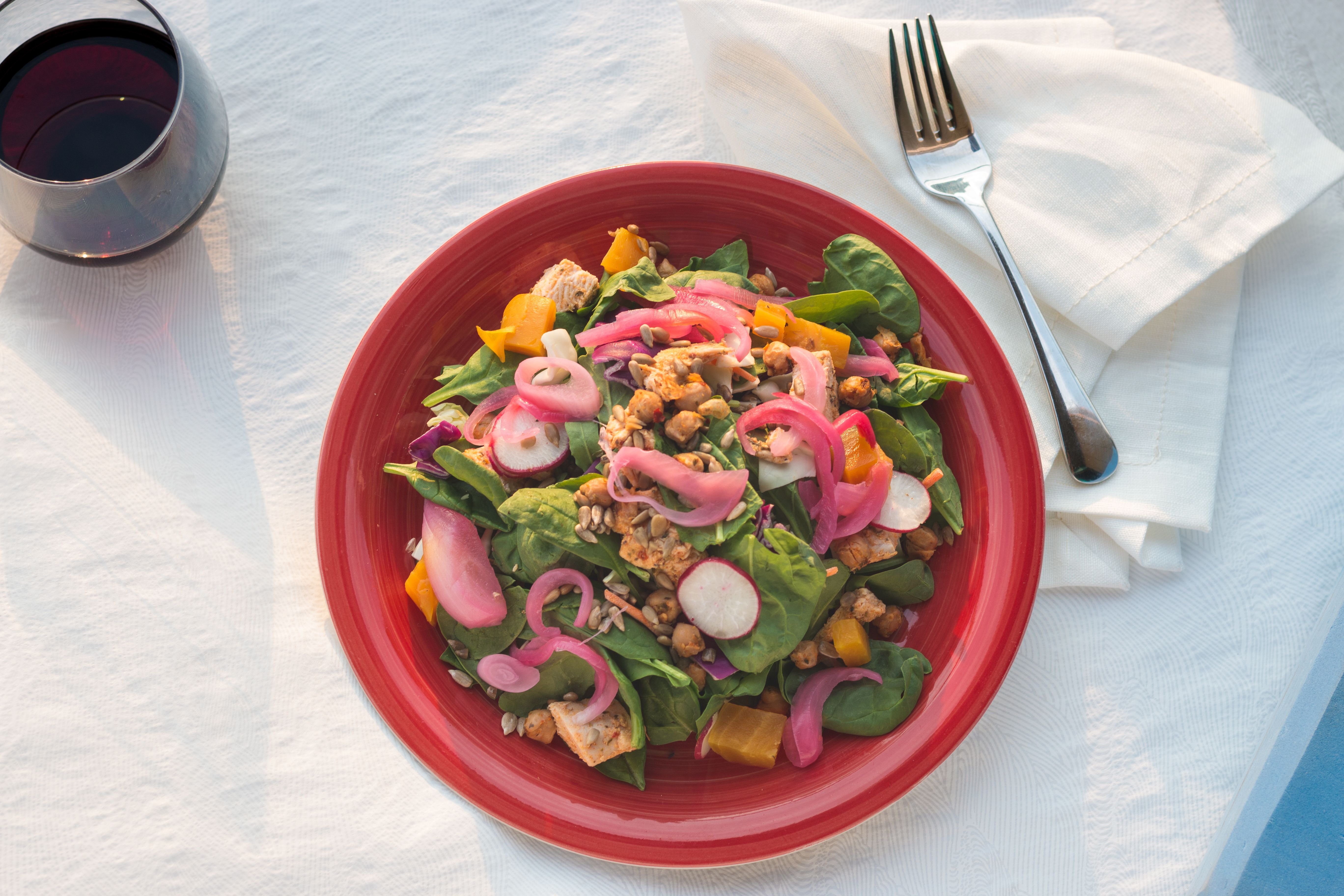 Delicious spinach salad with radishes, chickpeas, and pickled onions on a red plate.