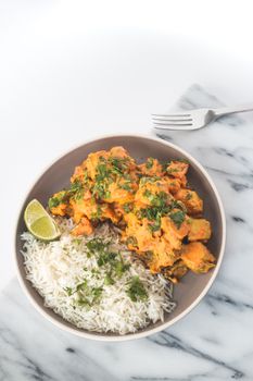 Close-up of a butter chicken meal with rice garnished with lime and herbs.