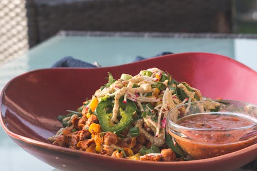 Delicious fresh salad topped with jalapenos and served with a side of spicy salsa in a stylish red bowl.