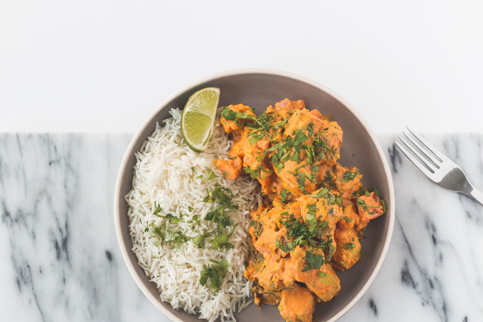 Golden curry chicken with tender potatoes served over white rice in a blue bowl, garnished with fresh thyme sprigs