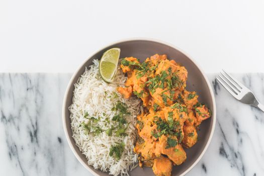 A vibrant chicken curry paired with basmati rice garnished with herbs and lime.