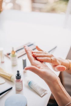 A woman rubs hand cream into her skin surrounded by beauty products on a table.