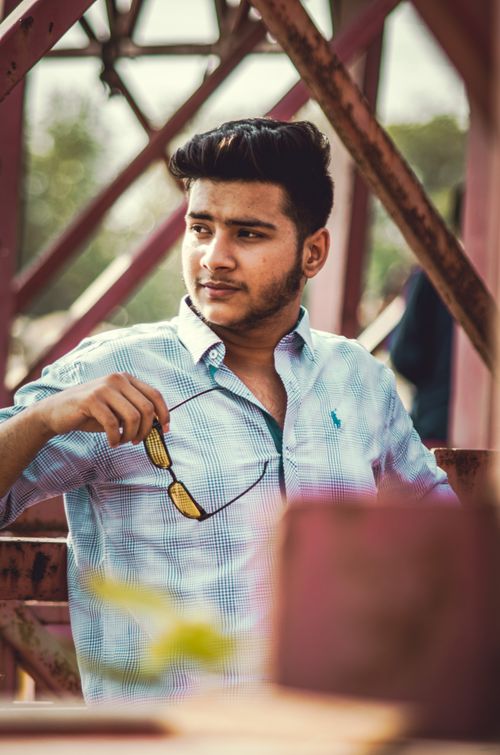 Free Portrait of a young man with sunglasses sitting outdoors, showcasing casual fashion style. Stock Photo