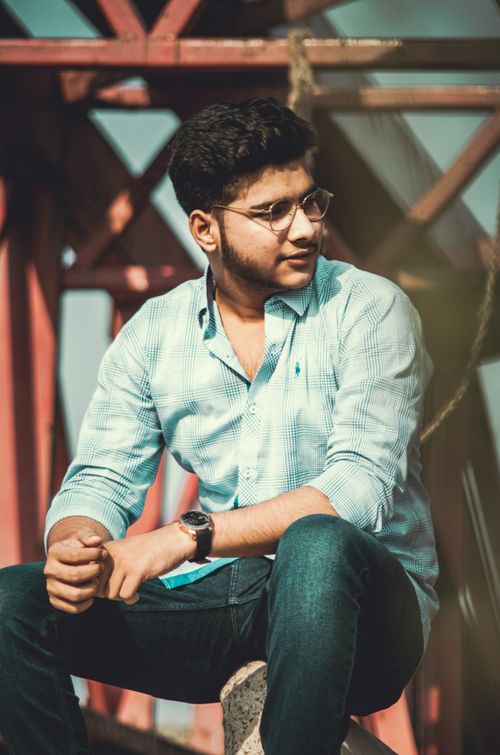 Free Portrait of a young man with eyeglasses in blue shirt, sitting outdoors on a concrete bench. Stock Photo