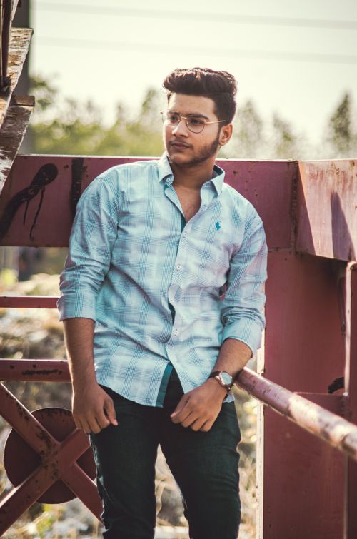 Free Young man in a light blue shirt leaning against a structure outdoors on a sunny day. Stock Photo