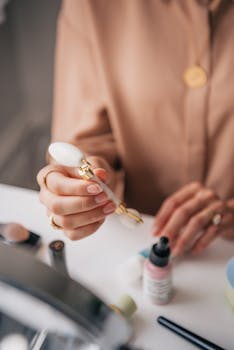 Close-up of a woman using a facial roller with skincare products on a table.