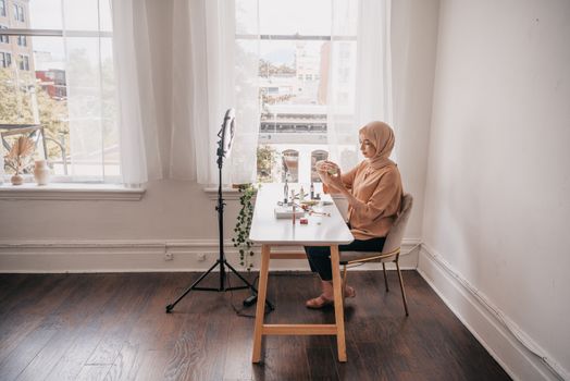 Muslim woman in hijab prepares cosmetics for streaming video indoors.