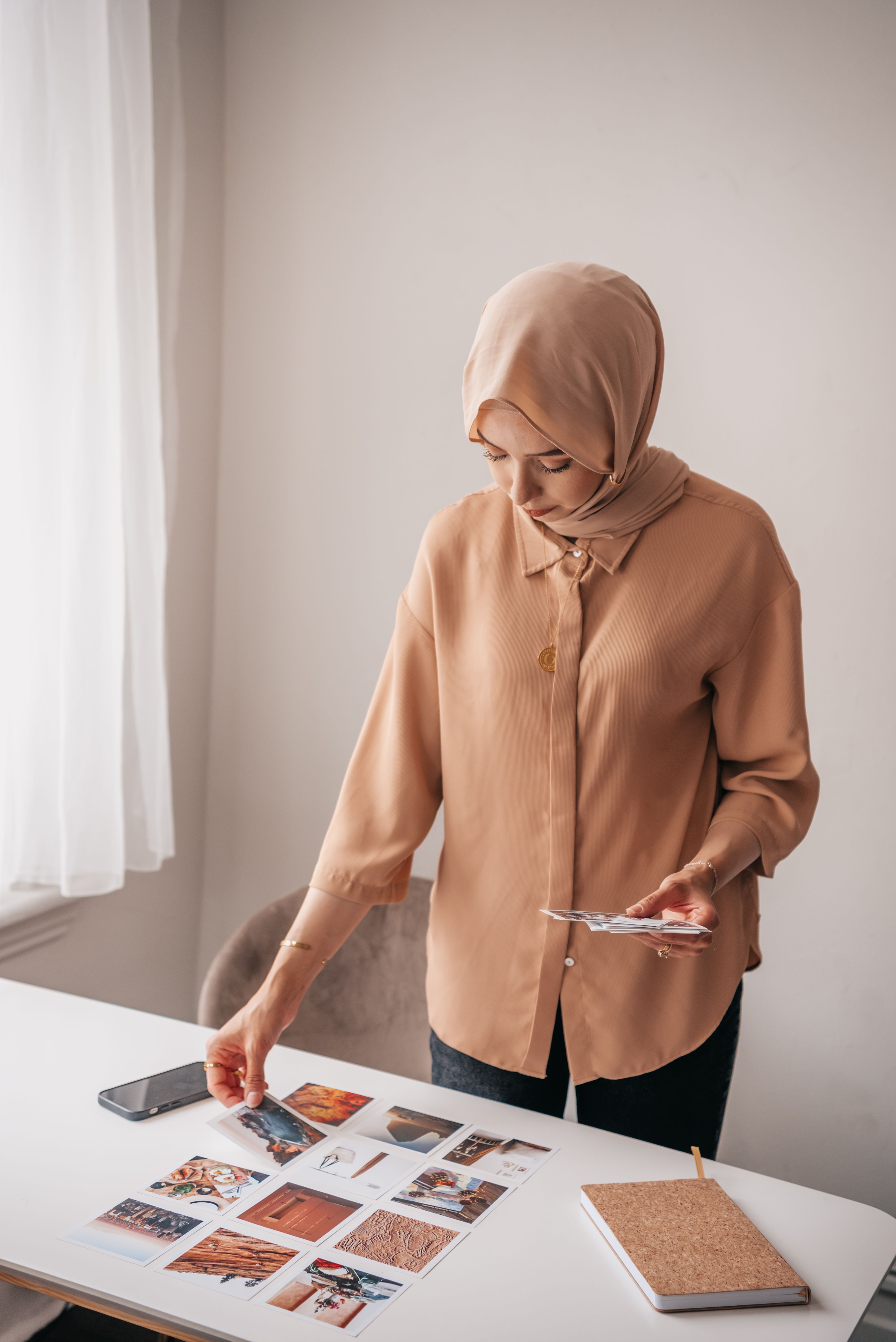 A young woman in hijab examines art prints at a desk in an office setting.