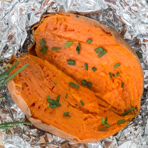 Free Close-up of a delicious baked sweet potato garnished with fresh chives on aluminum foil. Stock Photo
