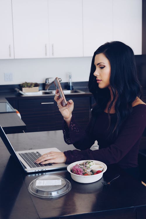 Woman with Laptop Looking at Cellphone