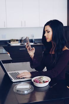 Young woman multitasking with laptop and smartphone while having a salad at home.
