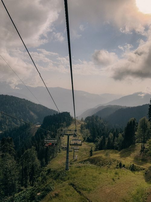 Free From above of cable railway over green hills covered with lush trees and plants under cloudy blue sky Stock Photo