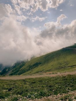Picturesque view of green mount slope covered with green grass under cloudy blue sky in daytime
