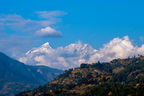 Free Beautiful view of snow-capped Himalayan peaks surrounded by clouds and lush green hills under a clear blue sky. Stock Photo