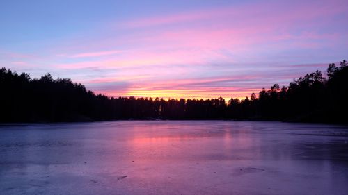 Free A breathtaking view of a winter sunset casting vibrant colors over a frozen lake and silhouetted forest. Stock Photo