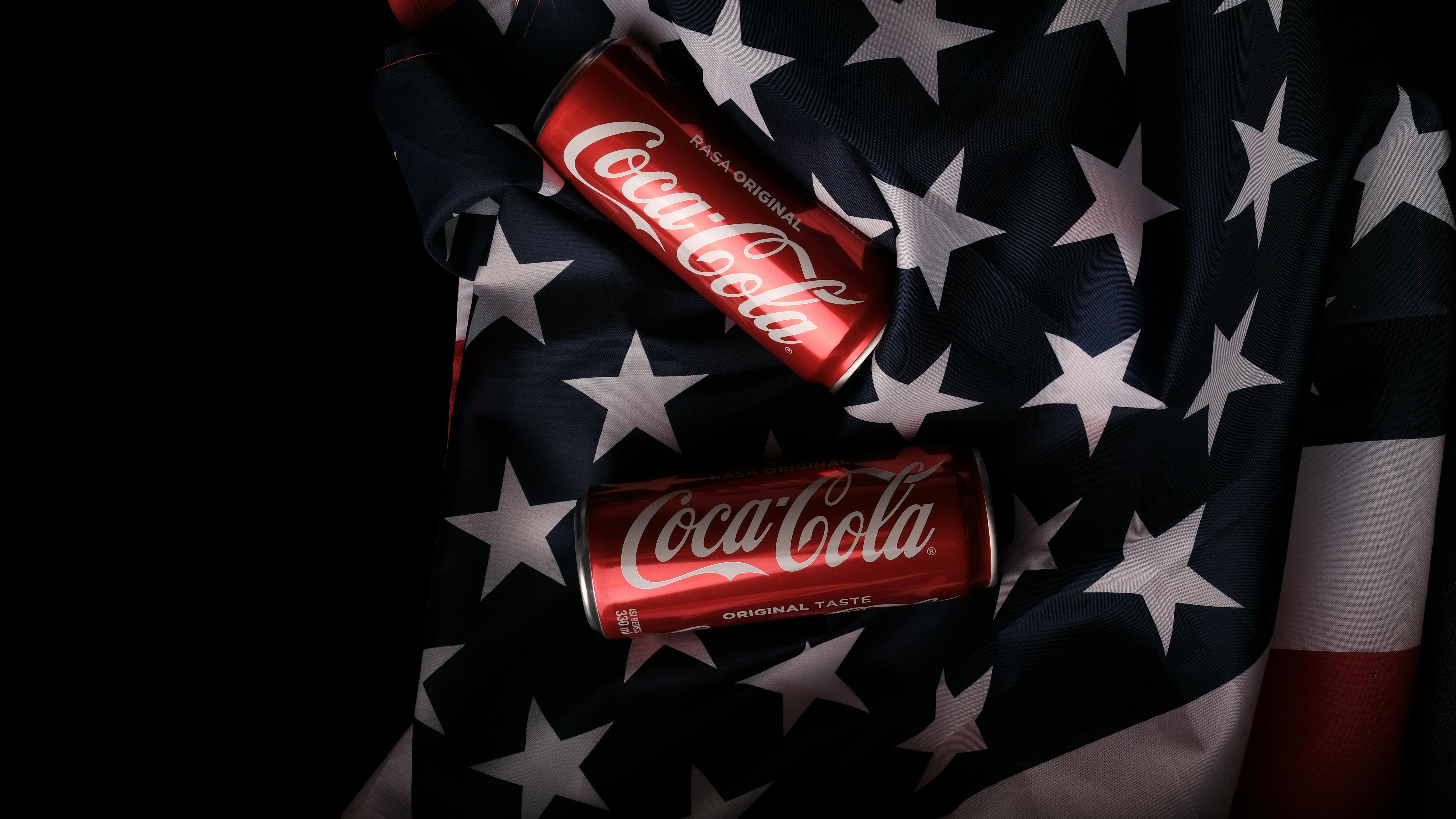 Red Coca Cola cans displayed on an American flag indicating patriotism and brand recognition