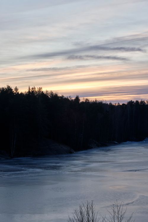 Free A tranquil sunrise over a frozen lake surrounded by dense forest, capturing nature's serenity. Stock Photo