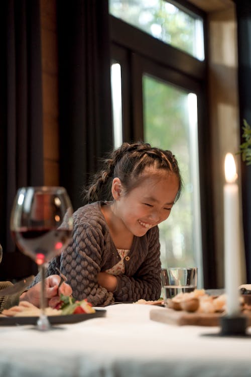 A Young Girl Looking at the Drinking Glass on the Table while Smiling